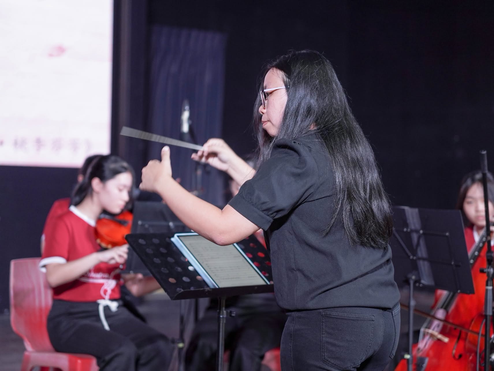 弦乐团教练指导学生进行演出，专注投入地挥动指挥棒，引领团员默契合奏，为教师节庆典呈现精彩的音乐演出。